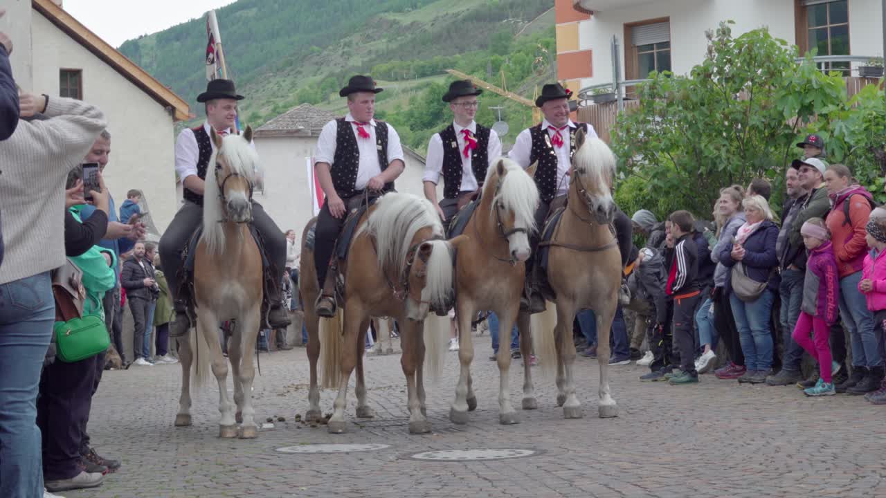 Men in Traditional Attire Riding Haflinger Horses in a Village Parade