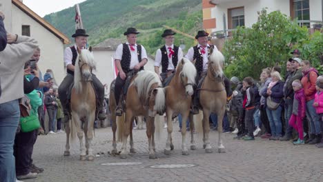 men in traditional attire riding haflinger horses in a village parade