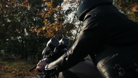 Rückansicht-Eines-Mannes-Mit-Schwarzem-Helm-Und-Lederjacke,-Der-An-Einem-Sonnigen-Herbsttag-Auf-Einer-Asphaltstraße-Motorrad-Fährt.-Bäume-Mit