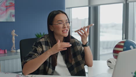 Mujer-De-Anteojos-Charlando-Con-Teléfono-Inteligente-En-El-Primer-Plano-De-La-Oficina.-Señora-Asiática-Hablando-Por-Teléfono