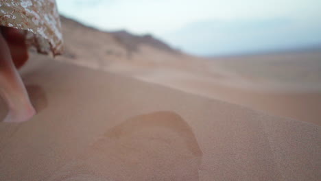 slow motion feet close-up: woman in dress walks on desert sand dune