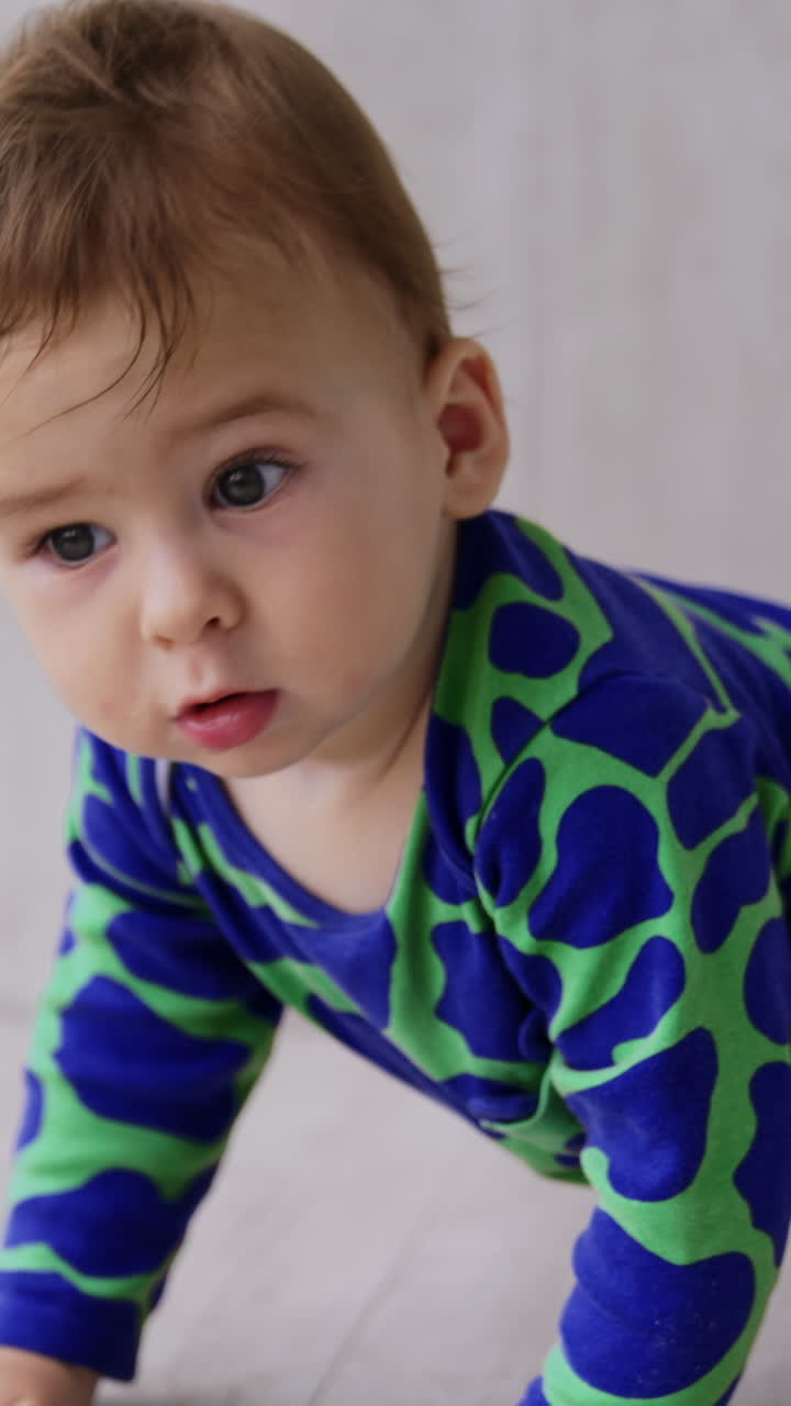 Sweet toddler boy crawling on the floor by the panoramic window. Close up. Ball at the backdrop in blur. Vertical video