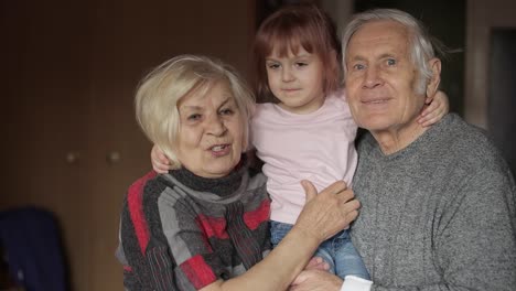 Granddaughter-kissing-senior-smiling-grandfather-with-grandmother-at-home