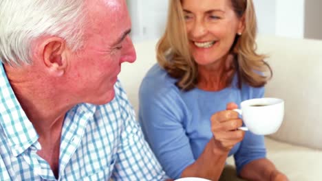 Una-Pareja-De-Ancianos-Sonriente-Interactuando-Mientras-Toma-Una-Taza-De-Café-En-La-Sala-De-Estar