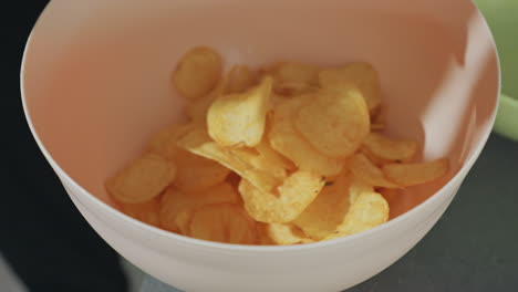 close up of bowl with potato chips snack on kitchen counter, golden crispy chips falling into bowl, crunchy tasty snack, home kitchen setting, casual food preparation, delicious snack