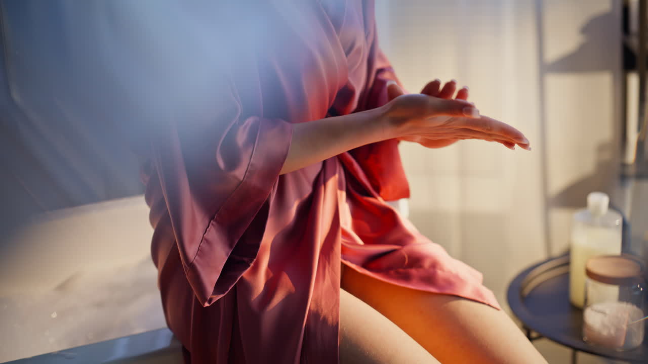 Primo piano di una donna che sprema la lozione nei palmi alla luce del mattino. Ragazza che applica la crema sulle gambe.