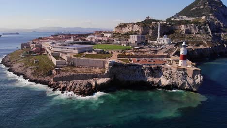 Strong-swell-creates-a-heady-sea-on-a-windless-summer-day-as-white-gulls-fly-around-the-Europa-point-lighthouse-in-Gibraltar-with-in-the-background-ships-at-the-anchorage