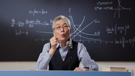 mathematics intelligent stylish teacher wearing eyeglasses explaining math formulas with chalk on green chalkboard in university or school classroom. education and studying video