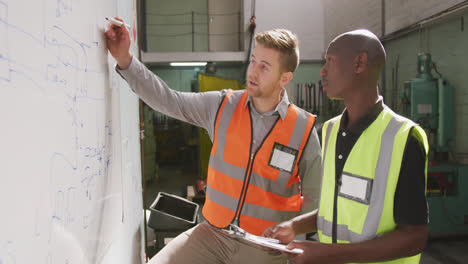 a caucasian and an african american male factory worker holding a clipboards