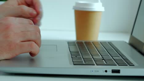 male hands on a laptop keyboard, an office worker takes a paper cup with coffee, drinks and puts it back