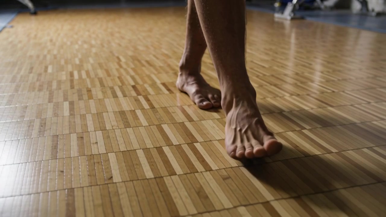 Spostando il peso, piedi di adulto che camminano dal tallone alla punta su un pavimento in parquet, mostrando la meccanica del piede.
