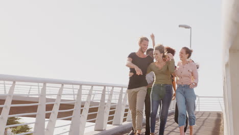 group of young friends outdoors walking across bridge together against flaring sun