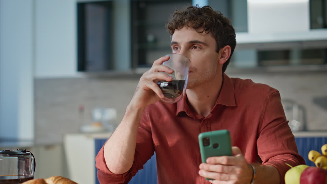 Cellphone man drinking coffee reading message at breakfast in kitchen closeup