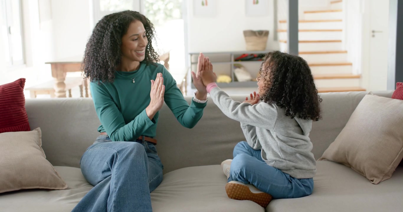 African American mother and child raising hands, teaching timing, clapping, high-fiving on sofa