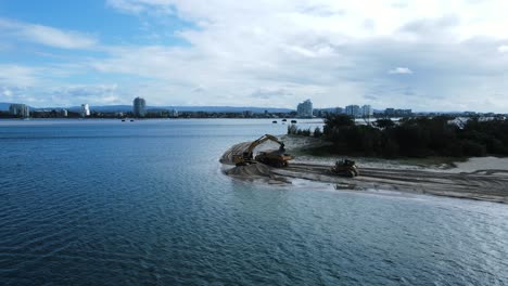 Vista-Panorámica-Sobre-El-Agua-De-Maquinaria-Grande-Trabajando-En-Una-Isla-De-Arena-Creando-Un-Nuevo-Puerto-De-La-Ciudad