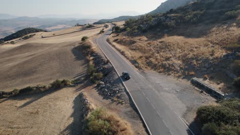 Luftdrohne-Schoss-über-Ein-Schwarzes-Auto,-Während-Sie-Abends-Durch-Die-Ländliche-Hügellandschaft-In-El-Torcal-De-Antequera,-Sierra-In-Spanien,-Fuhren