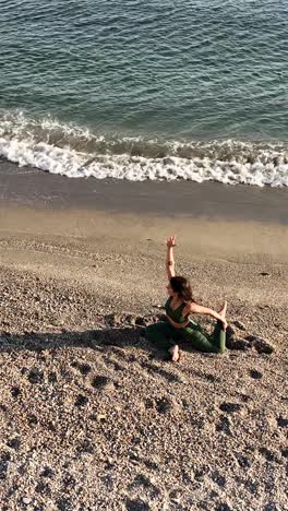 Fit female practicing seated yoga twist on sandy beach near wave