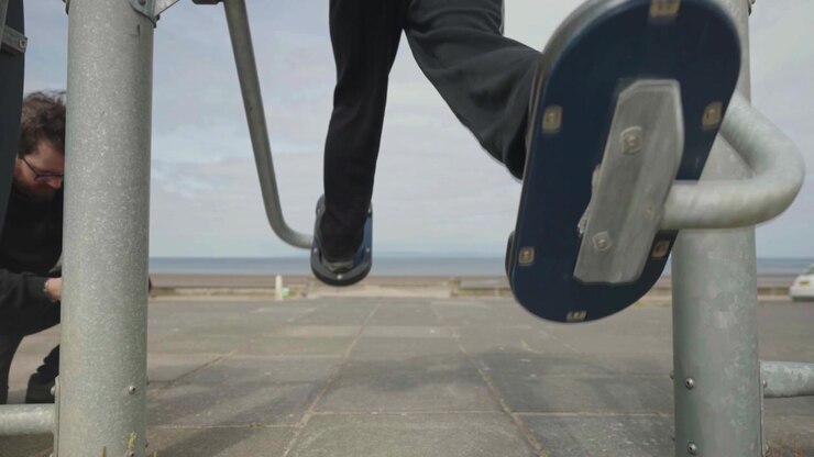 Man uses camera to capture movement of legs on exercise machine, slow mo