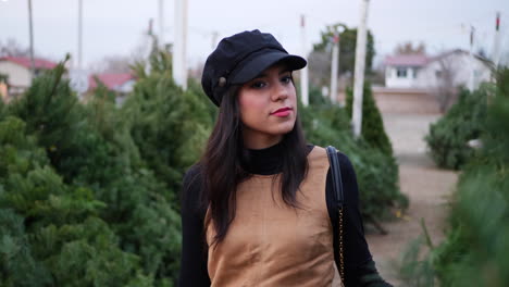 a hispanic woman shopping for a season holiday christmas tree on a lot with many species of fir trees