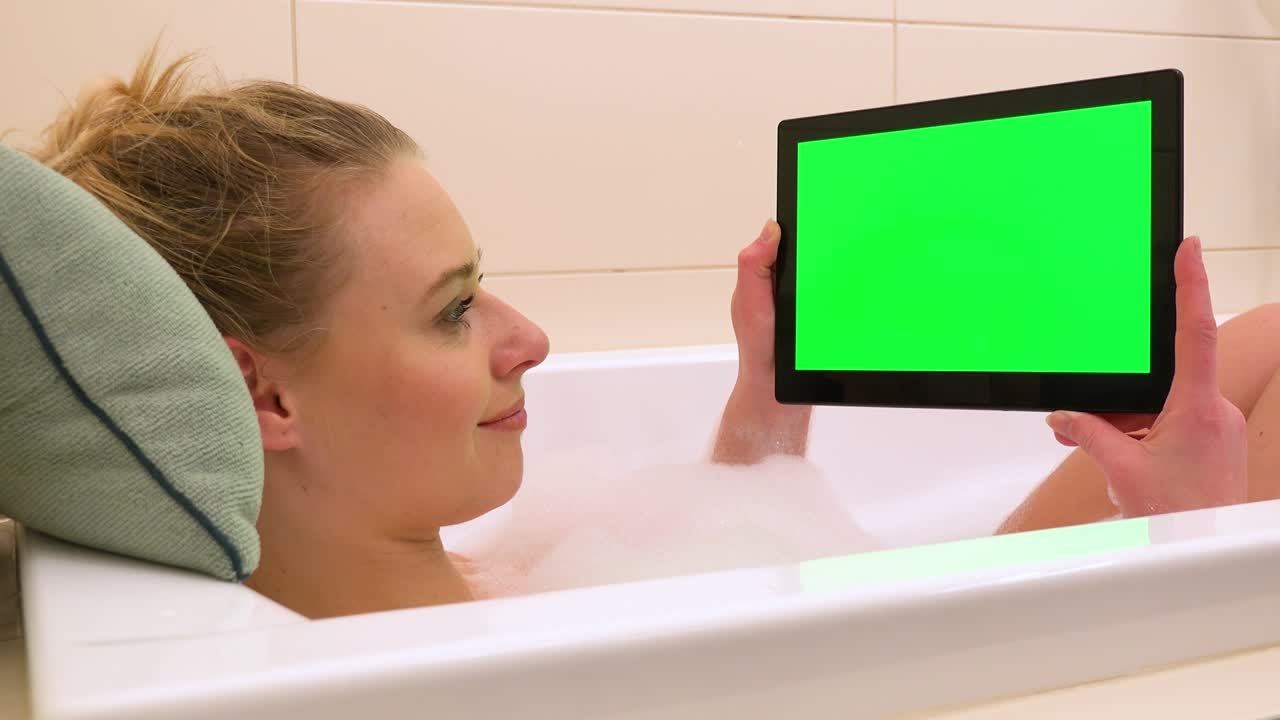 A young beautiful woman looks at a tablet with a green screen in a bathtub - closeup