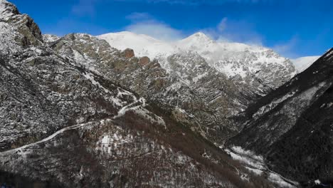 Aerial:-snowy-mountain-slope-with-snow-covered-mountains-in-the-background