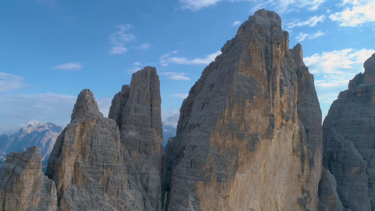 Orbiting aerial view flying close to Tre Cime sunlit mountain stone peaks against blue sky