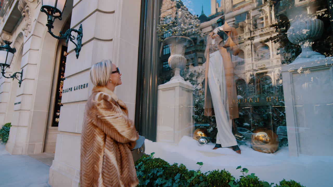 New York, USA, 25 ottobre 2025: Donna che guarda la vetrina di una boutique di lusso a Manhattan. Persona alla moda che osserva una vetrina di vendita al dettaglio a tema invernale su una strada elegante di New York