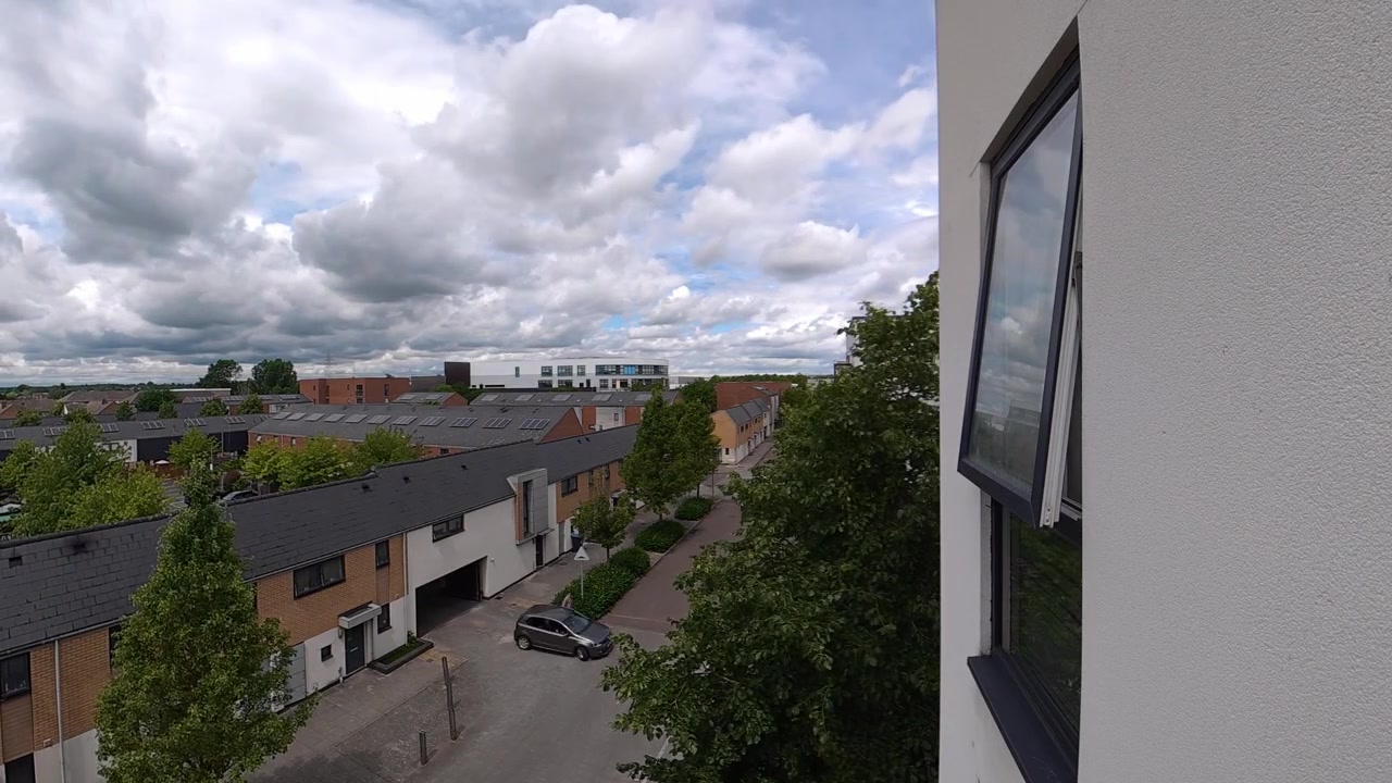 Timelapse av luftige hvite skyer som beveger seg over en blå himmel over et moderne boligområde med hus og trær.