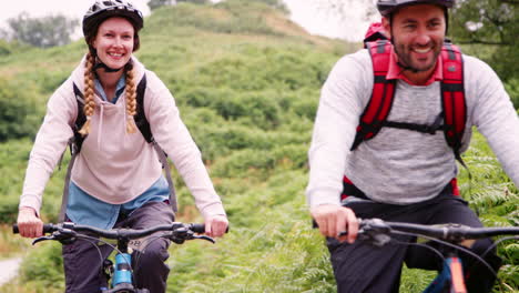 young adult couple riding mountain bikes in the countryside during a camping holiday, lake district, uk