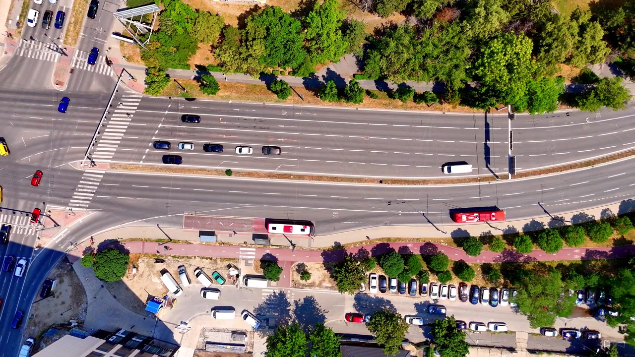 Perspectiva aérea de avenida de várias pistas, Bratislava, Eslováquia. Vista de drone de um ônibus vermelho e carros dirigindo em estrada de asfalto larga ao lado de árvores verdes.