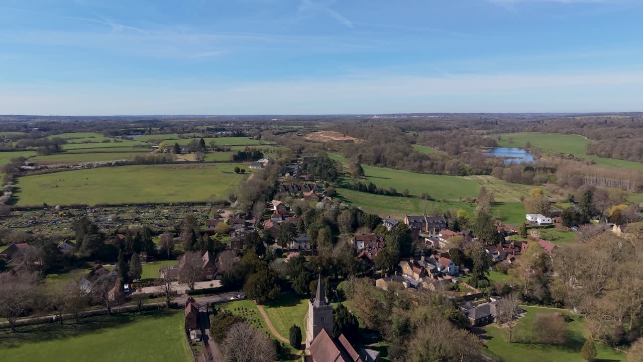 Hertingfordbury drone flight over St Mary's church and village, gliding toward Panshanger quarry on a bright spring day with green fields, countryside homes, and clear skies