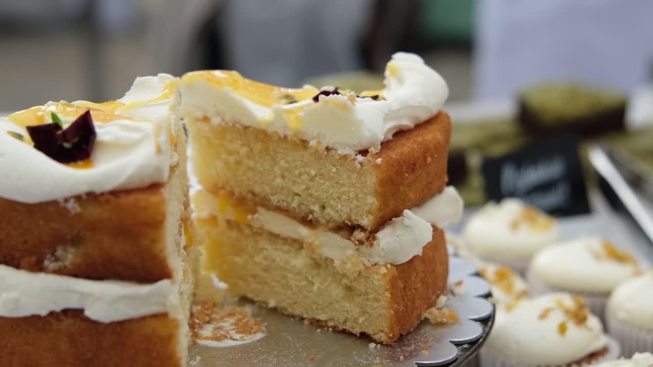A Victoria Sponge Cake on display for sale at local café market, with many different sweets and cakes in the background.