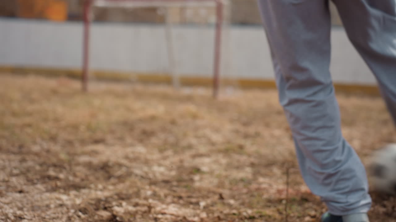 흰색 바지를 입은 선수가 작은 골대 근처에서 슛을 하기 전에 자세를 잡고 발의 위치를 조정하고 있습니다. 회색 바지와 운동화를 착용했고, 공은 다리 뒤에 있습니다. 경기 준비와 의도가 보이며, 커뮤니티 경기장 분위기가 느껴집니다.