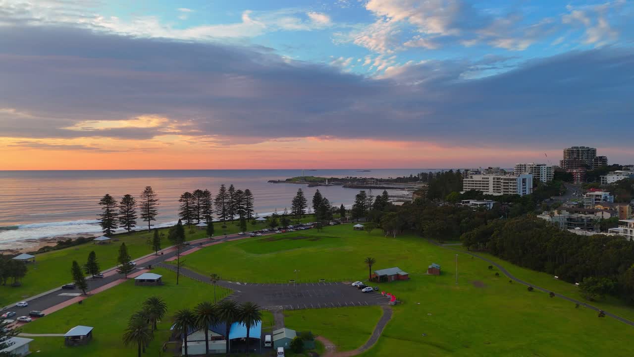 Aerial sunrise establishing of Wollongong city coastline and green parkland by sandy beach, quiet serenity