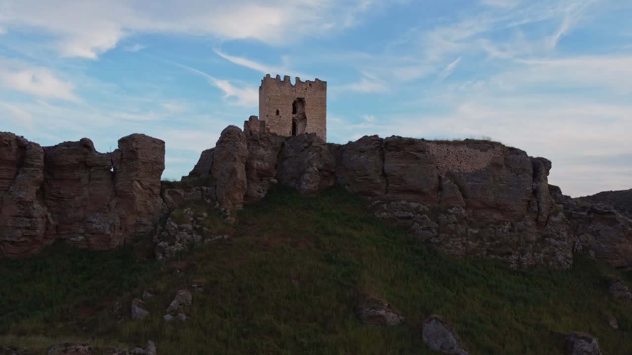 Reveal Drone shot of the medieval Oreja Castle perched on a hilltop at golden hour near Aranjuez, Spain. Scenic sunset over rural fields and rocky landscape.