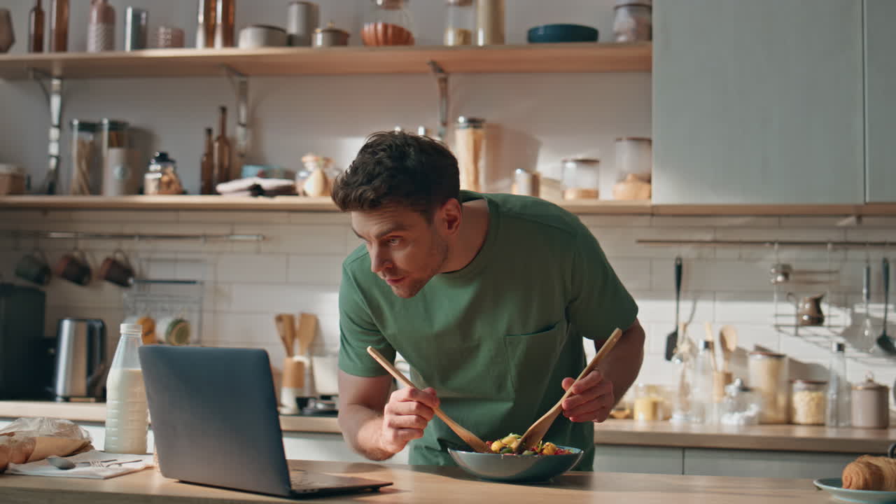 Young man watching video cooking in big kitchen closeup. Hipster looking laptop