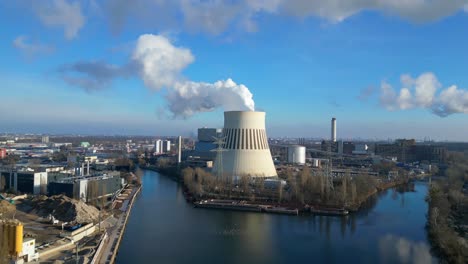 power plant emitting steam from its cooling tower, situated by a river and overlooking the cityscape. gorgeous aerial view flight ascending drone