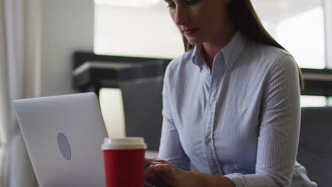 mujer caucásica haciendo papeleo usando una computadora portátil en la oficina