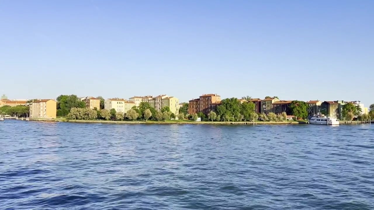 Vista dalla barca in movimento del lungomare di Sacca Fisola a Venezia, con edifici residenziali e infrastrutture lungo il canale.