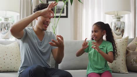 Happy-biracial-father-and-daughter-sitting-on-sofa-using-sign-language