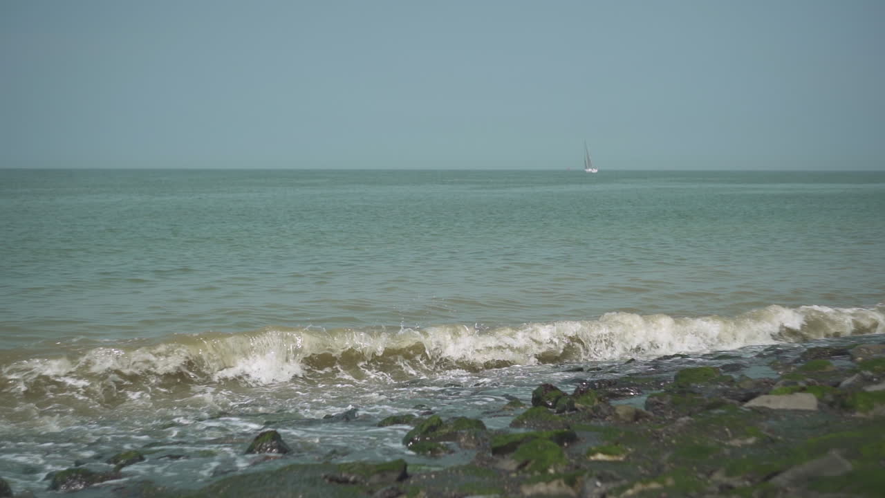 olas en la costa con un velero en el fondo, cámara lenta