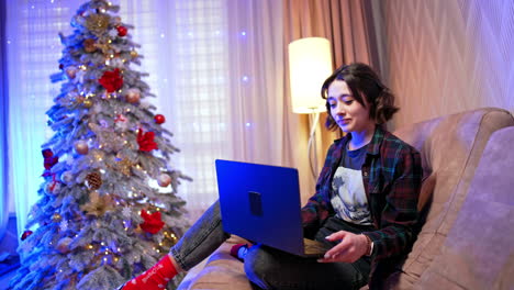 relaxing at home during the holidays. a cozy evening at home with festive decorations, a young person works on a laptop near a christmas tree