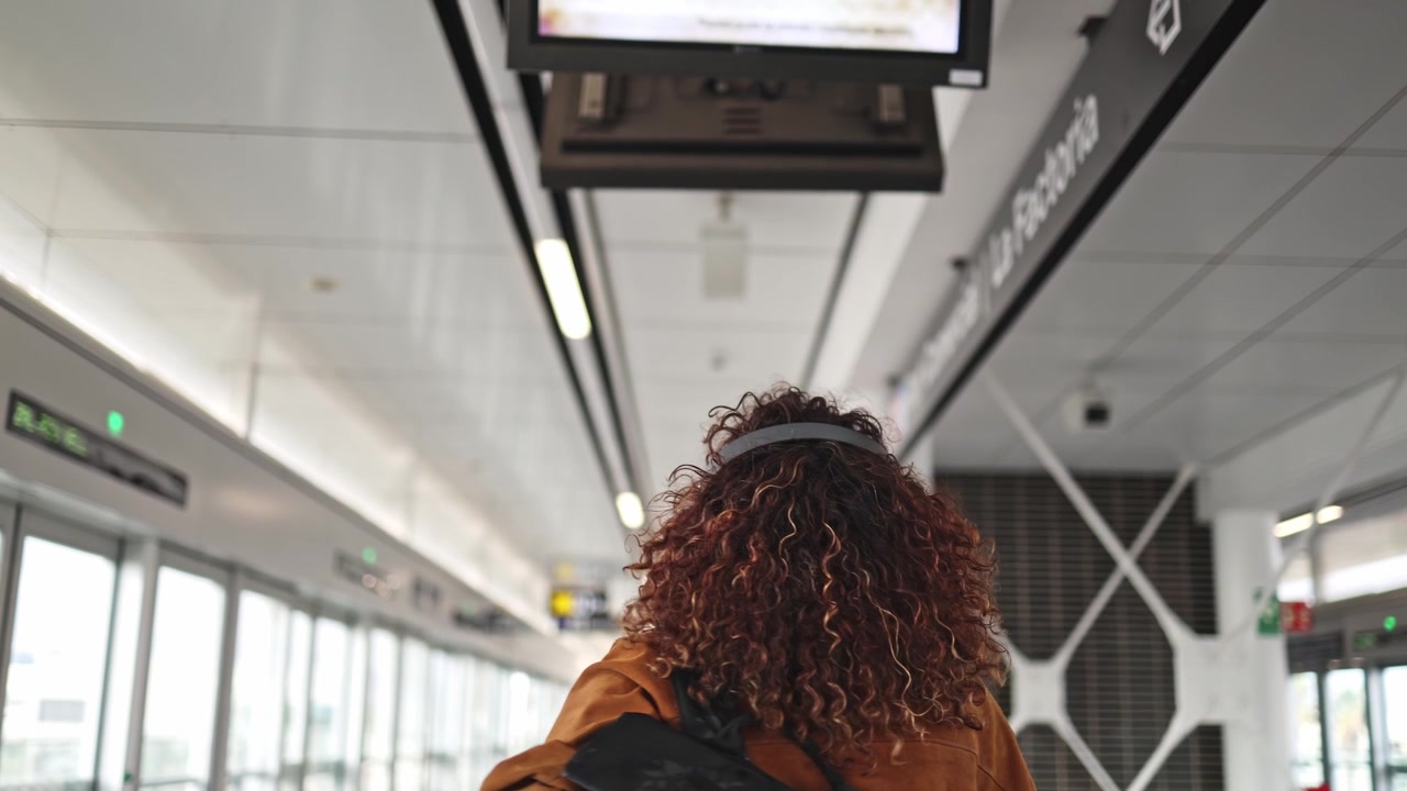 Mujer con cabello rizado y auriculares caminando en una estación de transporte público moderna