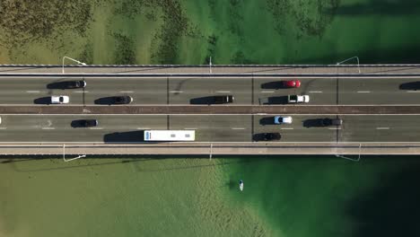 kayaks paddle under a busy urban city bridge spanning over clear ocean estuary waters