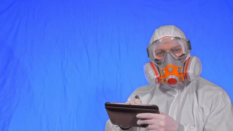 científico virólogo en respirador hace escribir en una tableta con lápiz. hombre con máscara médica de protección. clave de croma azul.