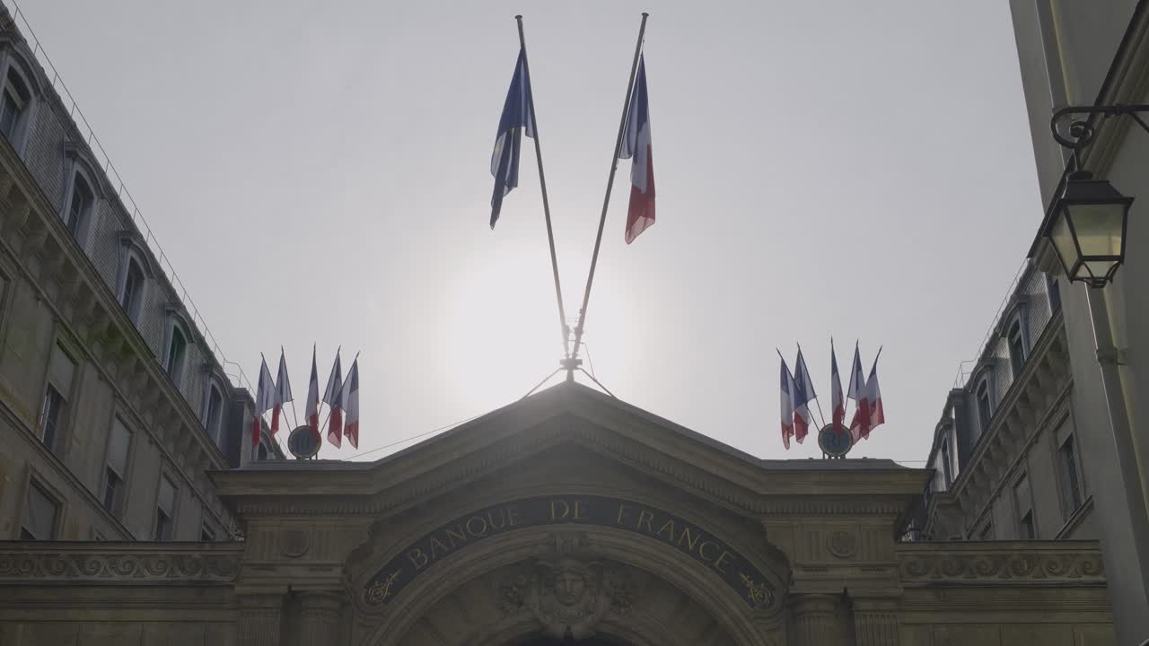 Building exterior of Banque de France in Paris with French flags under the sun