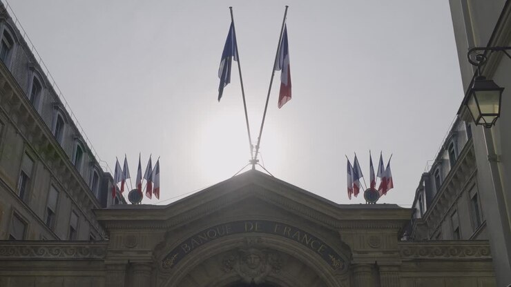 Building exterior of Banque de France in Paris with French flags under the sun