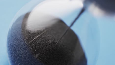 video of close up of hourglass with black sand pouring with copy space on blue background