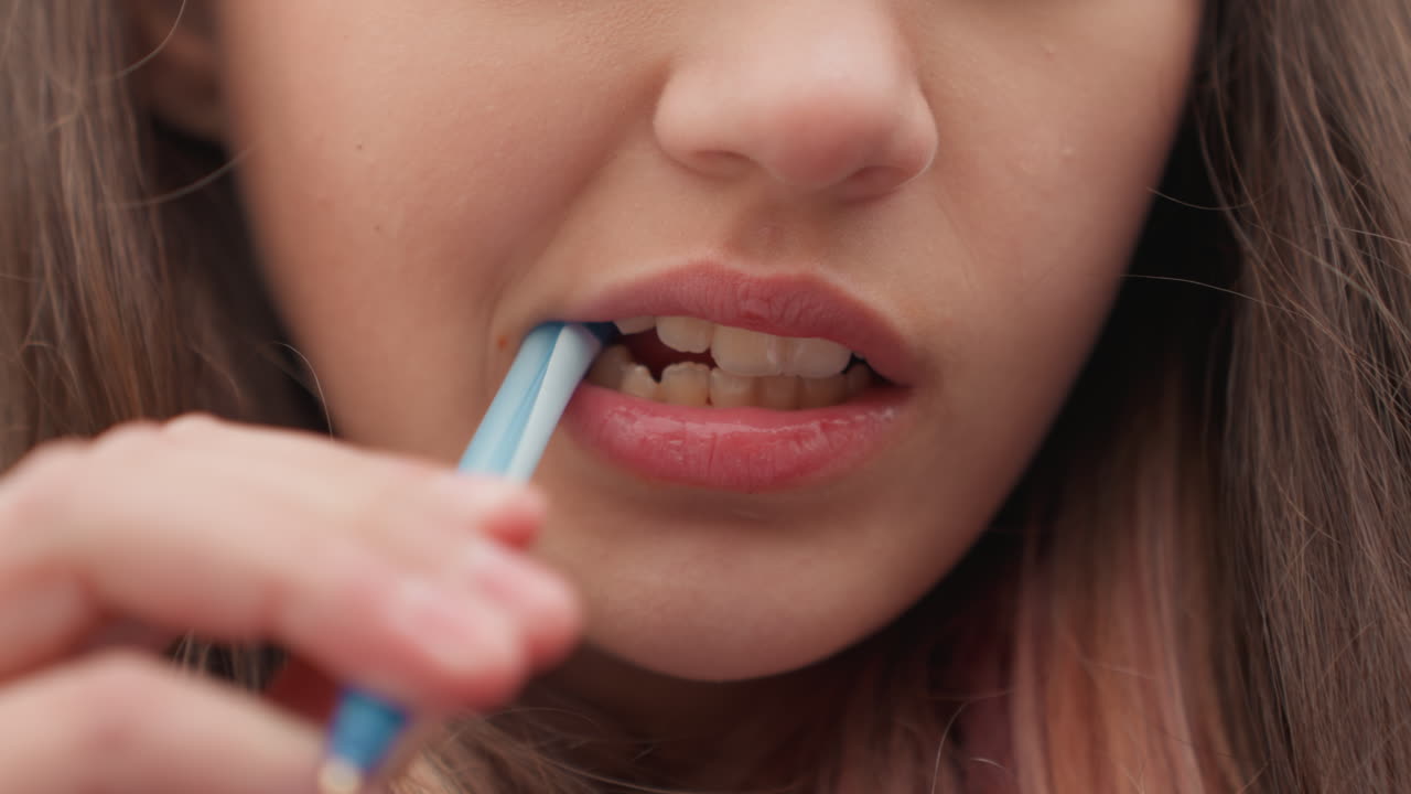 female student chewing pen cap closeup, anxious study moment during exam revision, bored expression with lip biting, fidgeting with stationery at desk, indoor classroom lighting, pensive gaze