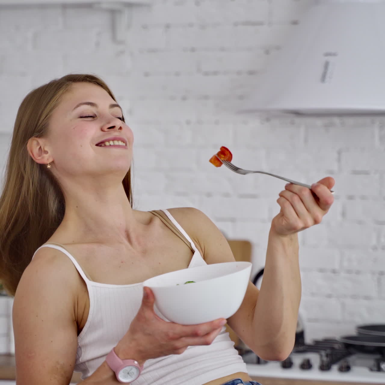 Young woman eating salad. Beautiful girl sniffing and eating organic vegetables on the kitchen background. Natural food concept.